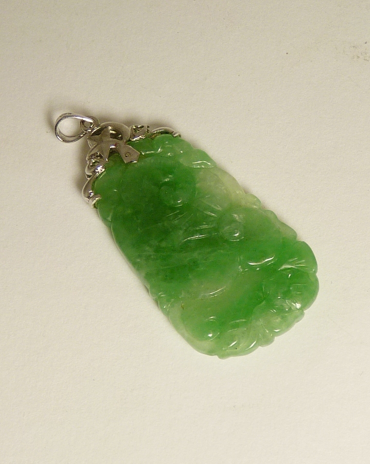 A carved green jade pendant piece with 22ct white gold openwork mount, the well-coloured jade