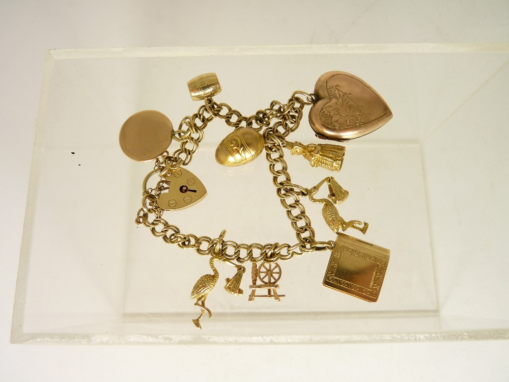 A 9ct gold padlock and link charm bracelet with attached 9ct gold charms including ; spinning wheel,