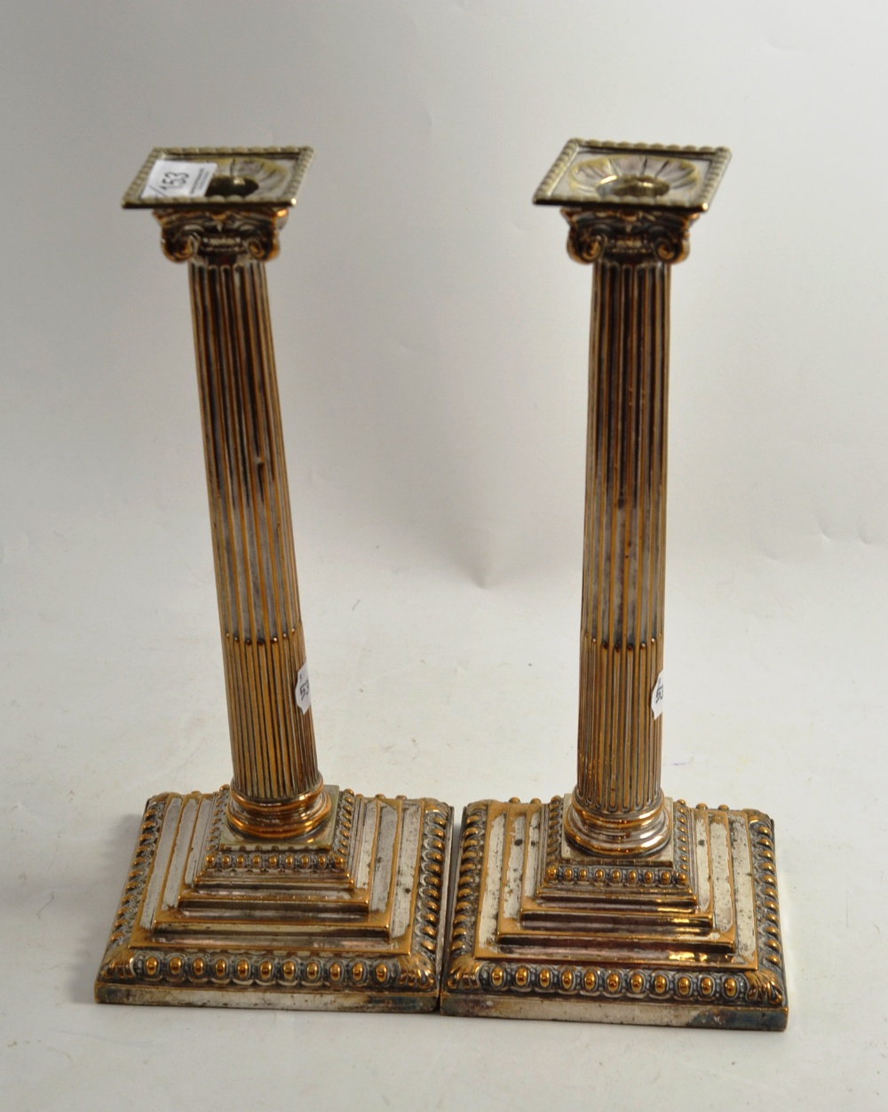 A pair of plated on copper Corinthian column table candlesticks with associated sconces