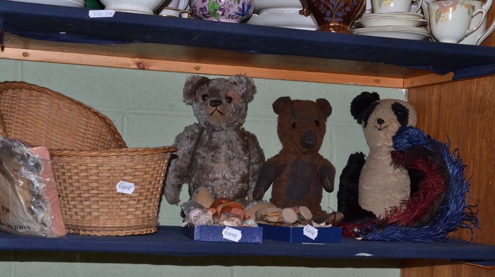 A shelf including two teddy bears, a panda, a wicker cradle, a composition doll, miniature dolls