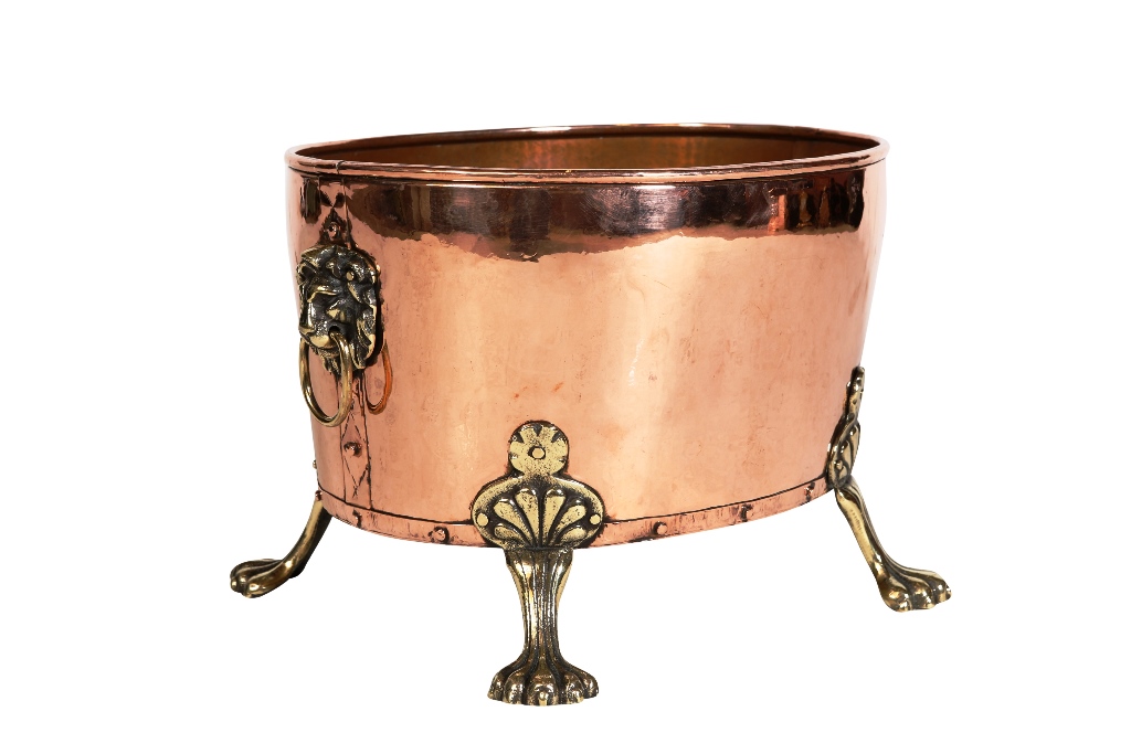 An early 20th century copper and brass jardiniere, oval, with lion mask ring handles, raised on