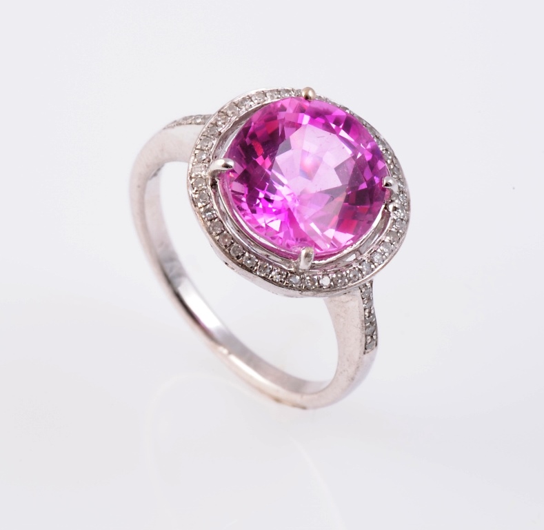 A pink sapphire ring, the round mixed cut pink sapphire four claw set within a channel set diamond