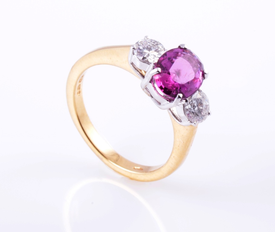 A ruby and diamond ring, the oval cut ruby four claw set above a pierced mount, set between a