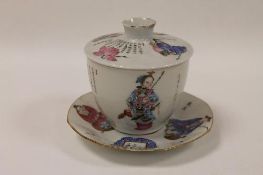 A Chinese famille rose lidded bowl and saucer, decorated with colourful panels depicting figures and