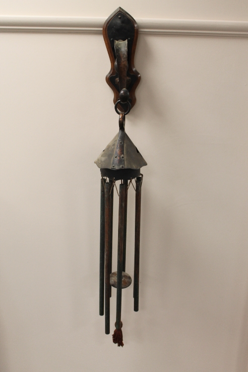 An Arts and Crafts copper wind chime, mounted on an oak bracket. CONDITION REPORT: Requires some