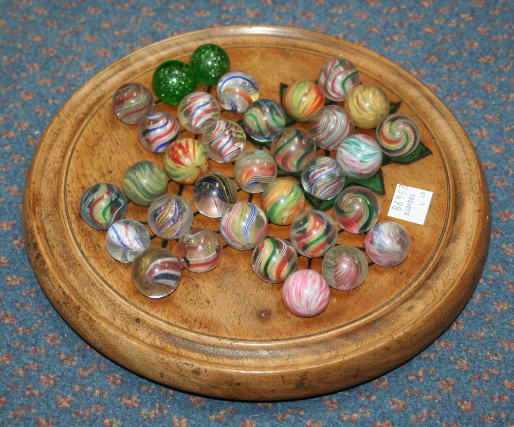 A solitaire board and marbles, including two green mica, coloured swirls and onion pattern (some