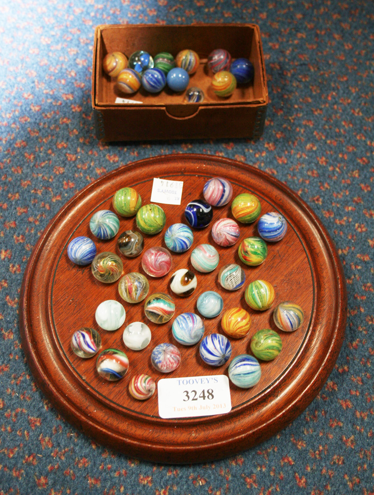 A mahogany solitaire board and a collection of marbles, including lattice, coloured swirls and