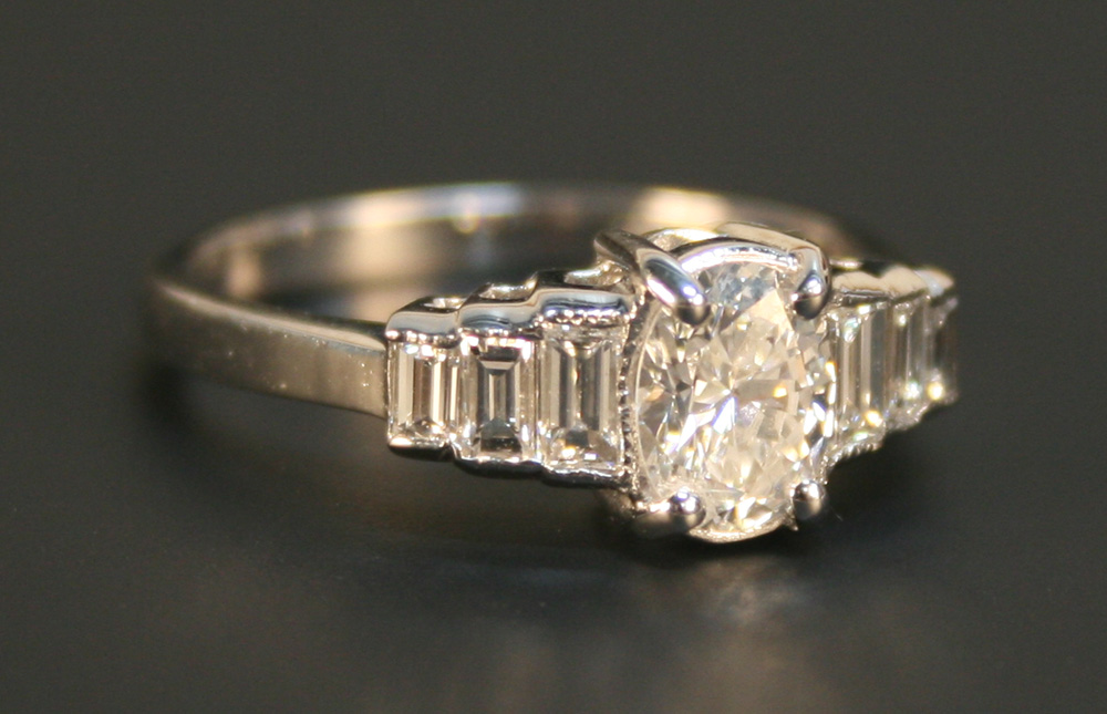 A diamond ring, claw set with the principal oval cut diamond between baguette diamond set stepped