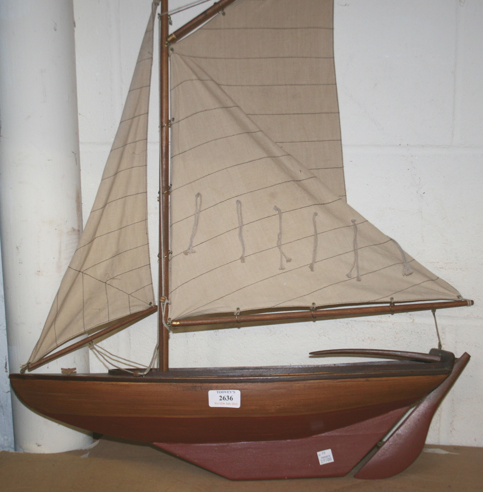 A mid-20th Century wooden pond yacht with single mast and cloth sails, half the hull painted in