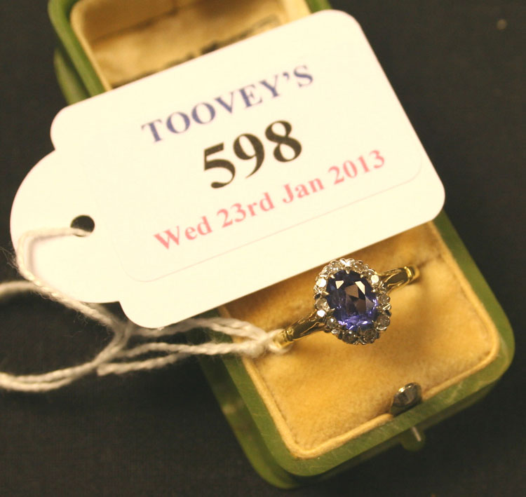 A gold, sapphire and diamond oval cluster ring, claw set with the oval cut sapphire within a