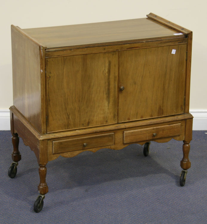 An early 20th Century walnut hostess trolley with extending top above cupboards and two drawers,