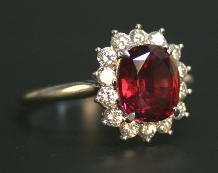 A garnet and diamond oval cluster ring, claw set with the oval cut garnet within a surround of