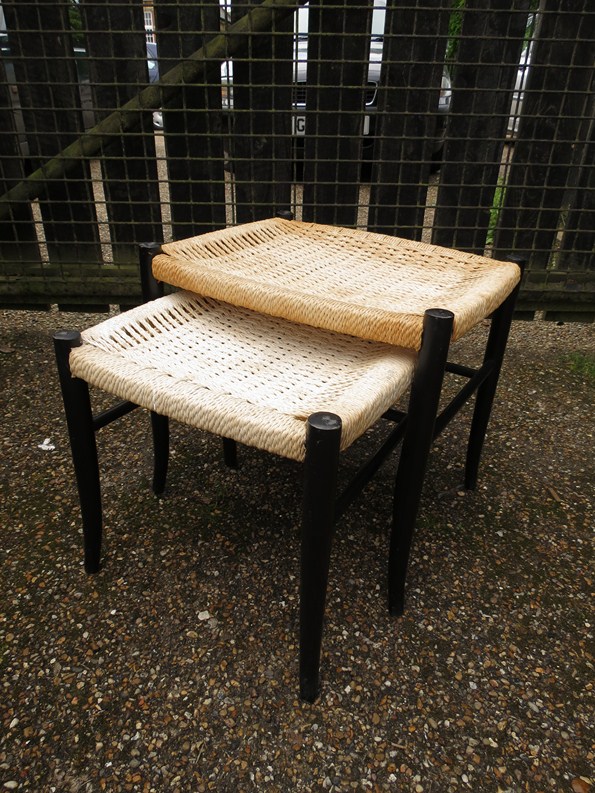 A nest of two ebonised stools with woven seats