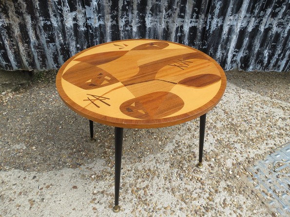 A 1960s circular coffee table with an abstract inlaid design top on ebonised legs