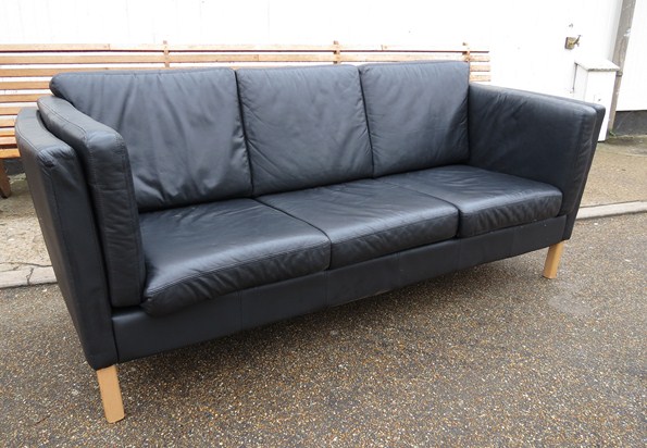 A black leather three seater Danish design sofa raised on squared legs.