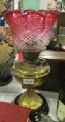 A brass oil lamp with cranberry glass shade