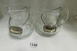 A pair of glass jugs with silver wine labels