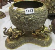 An embossed brass bowl surmounted by elephants