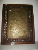 An Oriental brass plaque with ornate wood frame