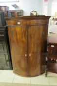 A Georgian mahogany bow front corner cupboard