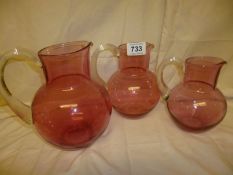 A set of 3 cranberry glass jugs