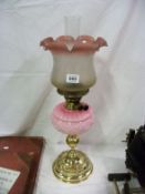 A victorian oil lamp with pink glass font on brass base and with later shade