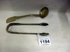 A pair of silver sugar tongs and a plated ladle