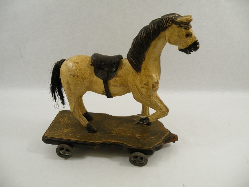 A folk art painted and carved wood horse, a pull-along toy with metal wheels 33cm high