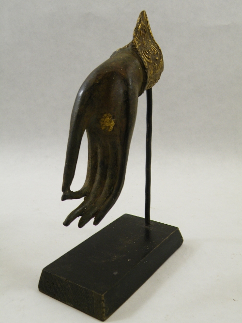 A bronze hand of Buddha in Varada Mudra pose, with traces of original gilding, on an ebonised wooden