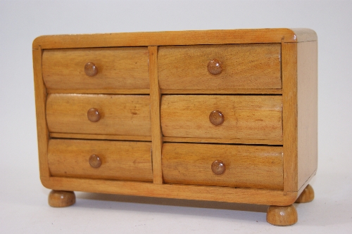 An Art Deco period miniature chest of drawers with six shaped drawer fronts and turned wooden