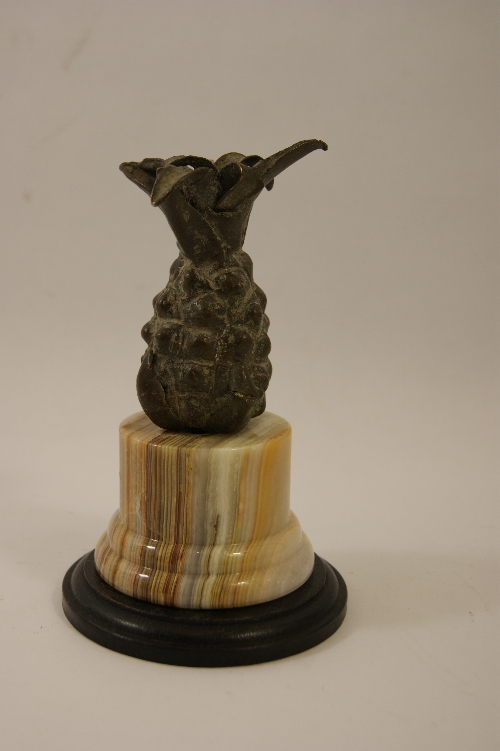 A bronze pineapple mounted on an onyx and ebonised wooden base 16cm high