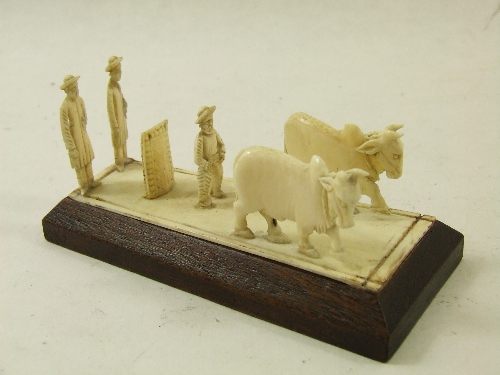 A late 19th C ornamental carved ivory group of men driving two buffalo on a shaped wooden base