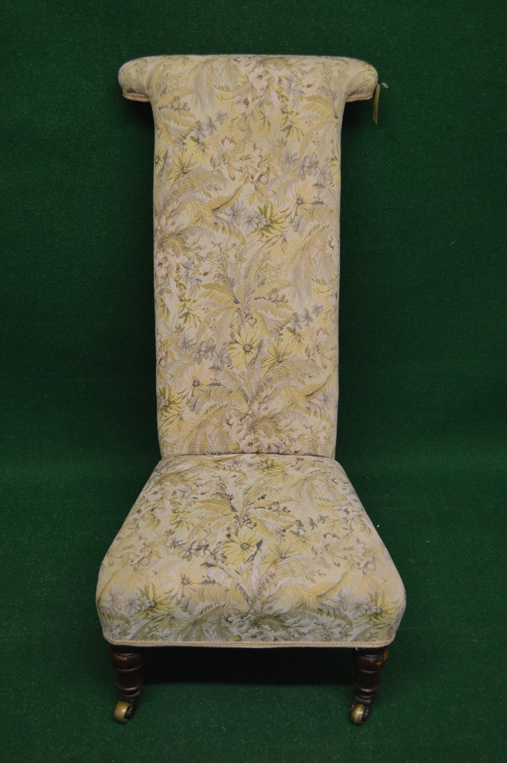 A prie dieu chair having floral upholstery and standing on turned legs ending i n brass castors