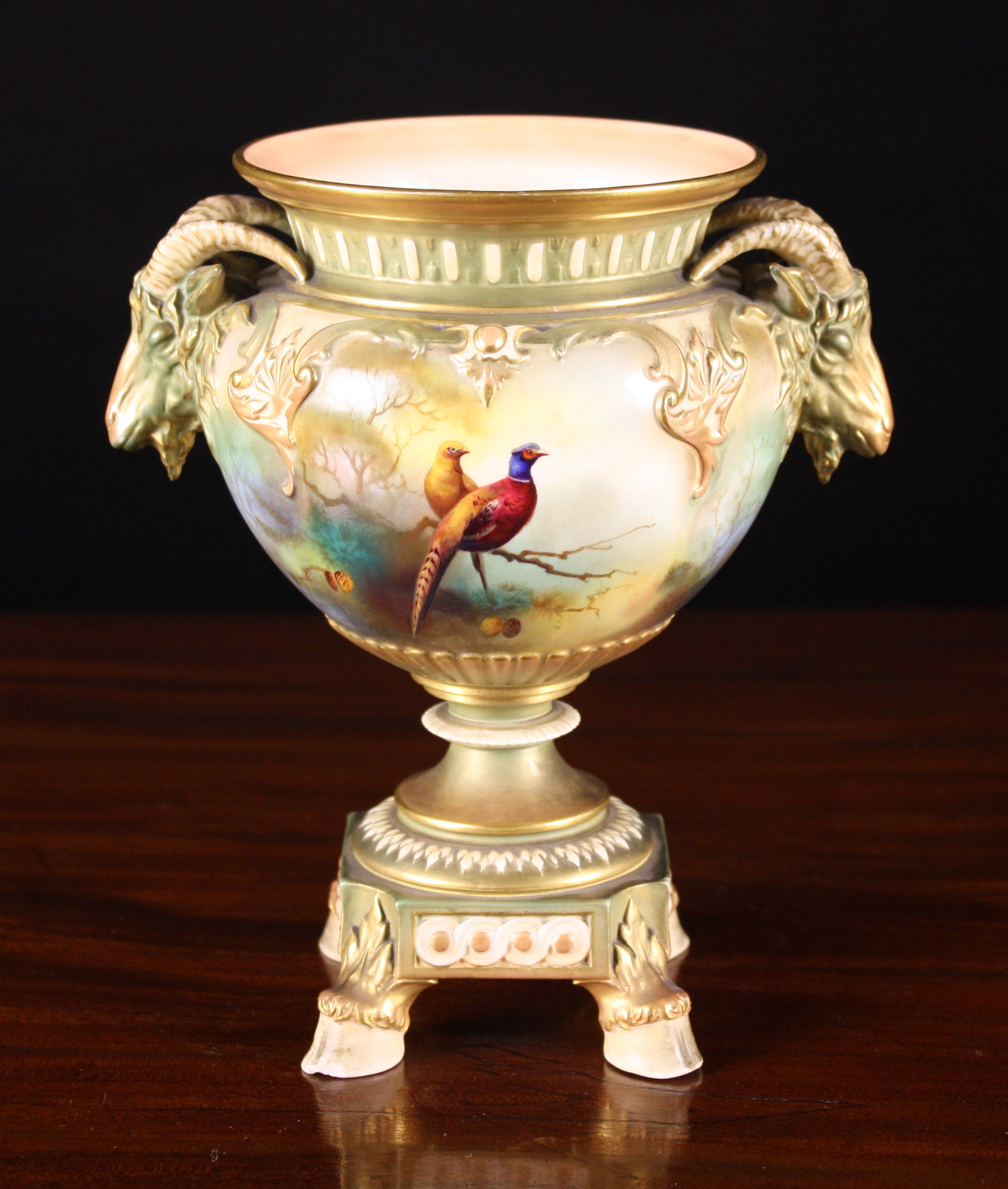 A Royal Worcester Urn with moulded rams' head handles.  The quatrefoil body painted with pheasants