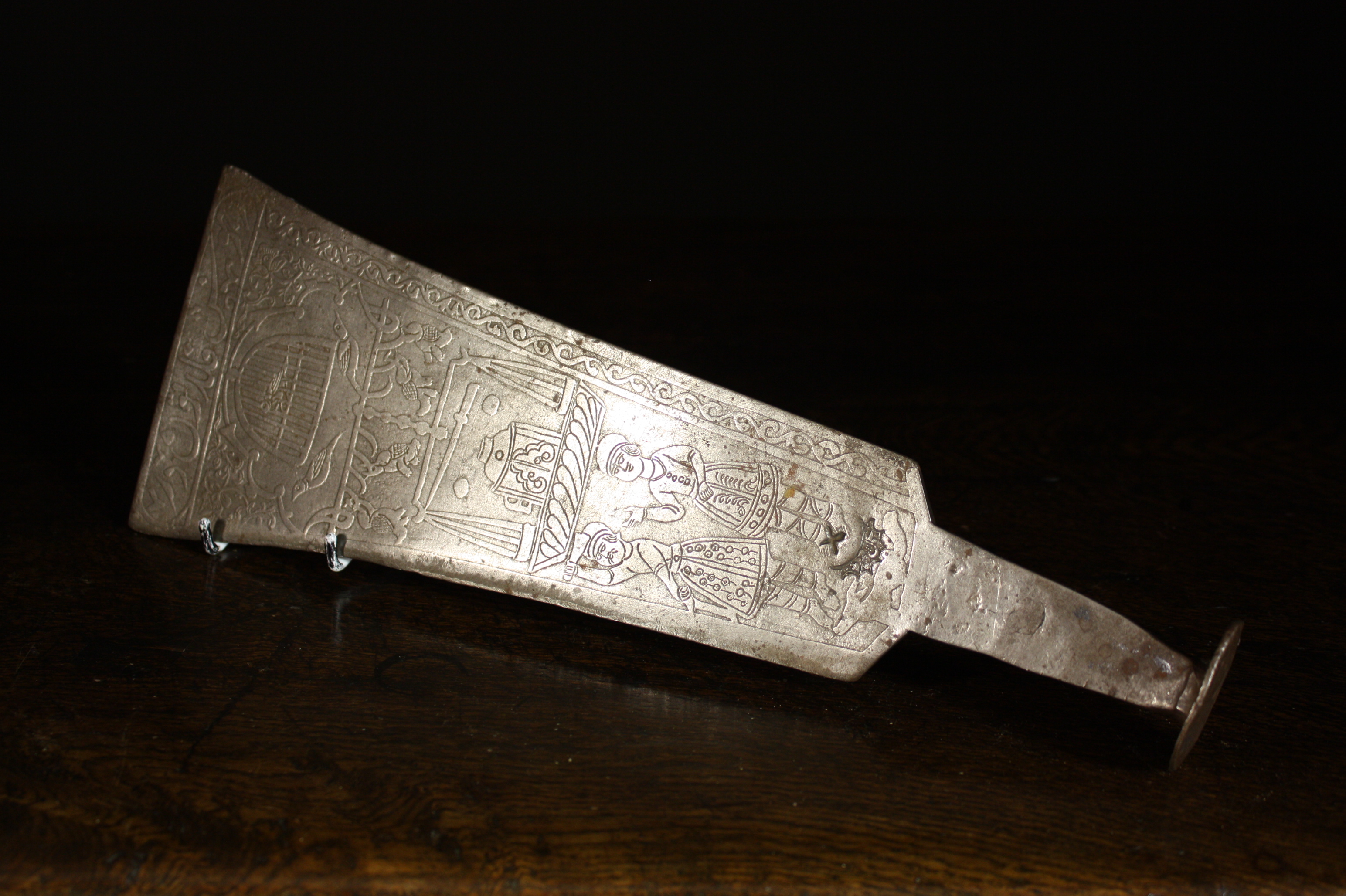 A Persian Steel Implement.  The flared flat-ended blade engraved with script above figures and