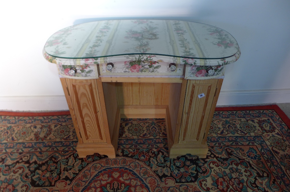 A small dressing table with upholstered drawers and shelves below together with its glass top