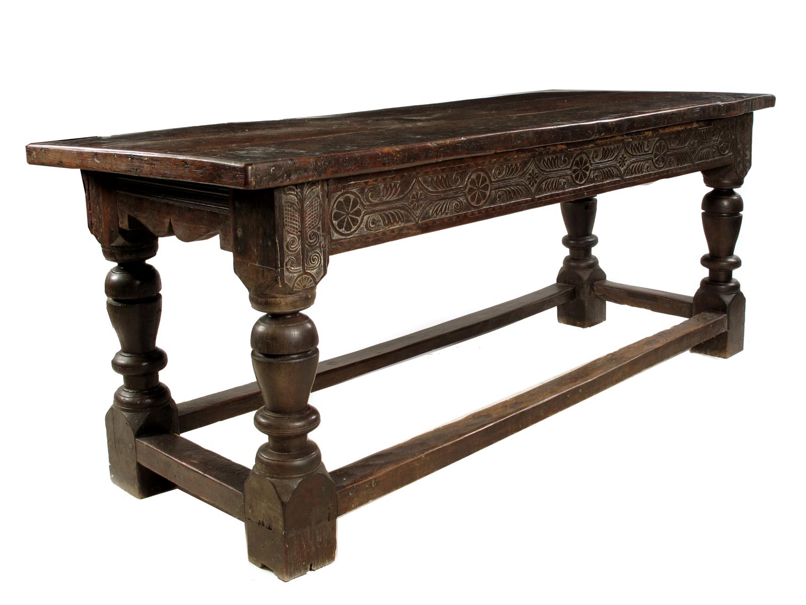 An oak refectory table, with a removable cleated end three board top, above a carved frieze having a