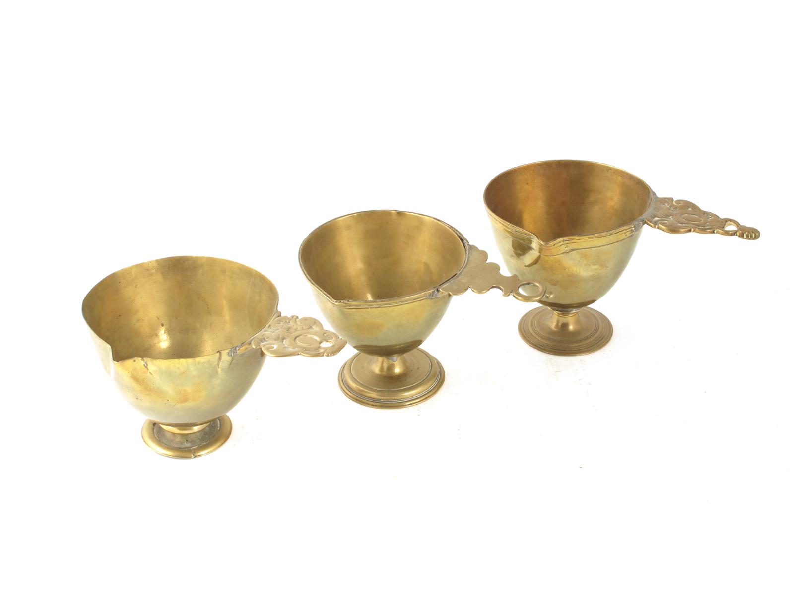 Three Dutch brass ecclesiastical spouted vessels, all with pierced handles, two with embossed