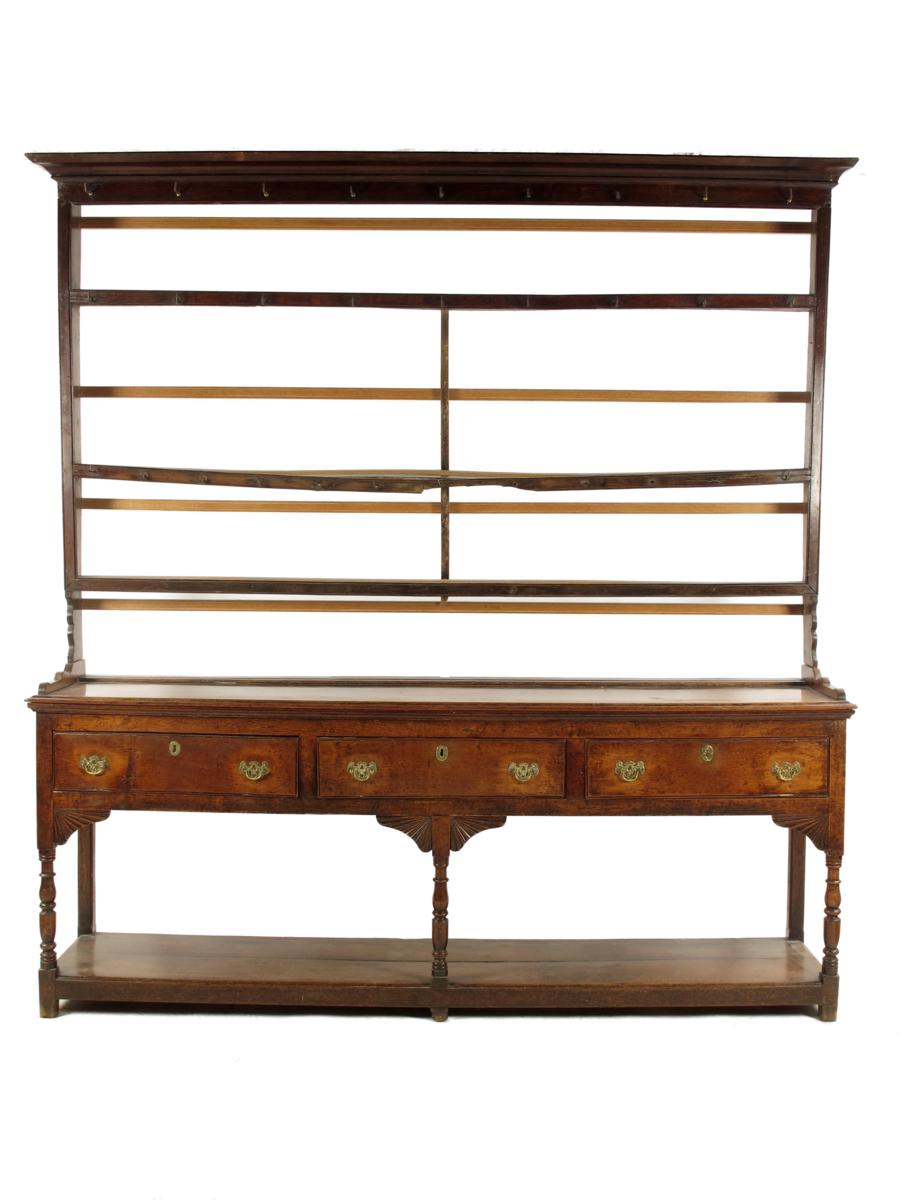 A late George III oak dresser, the open shelves with later brass hooks, above three frieze drawers