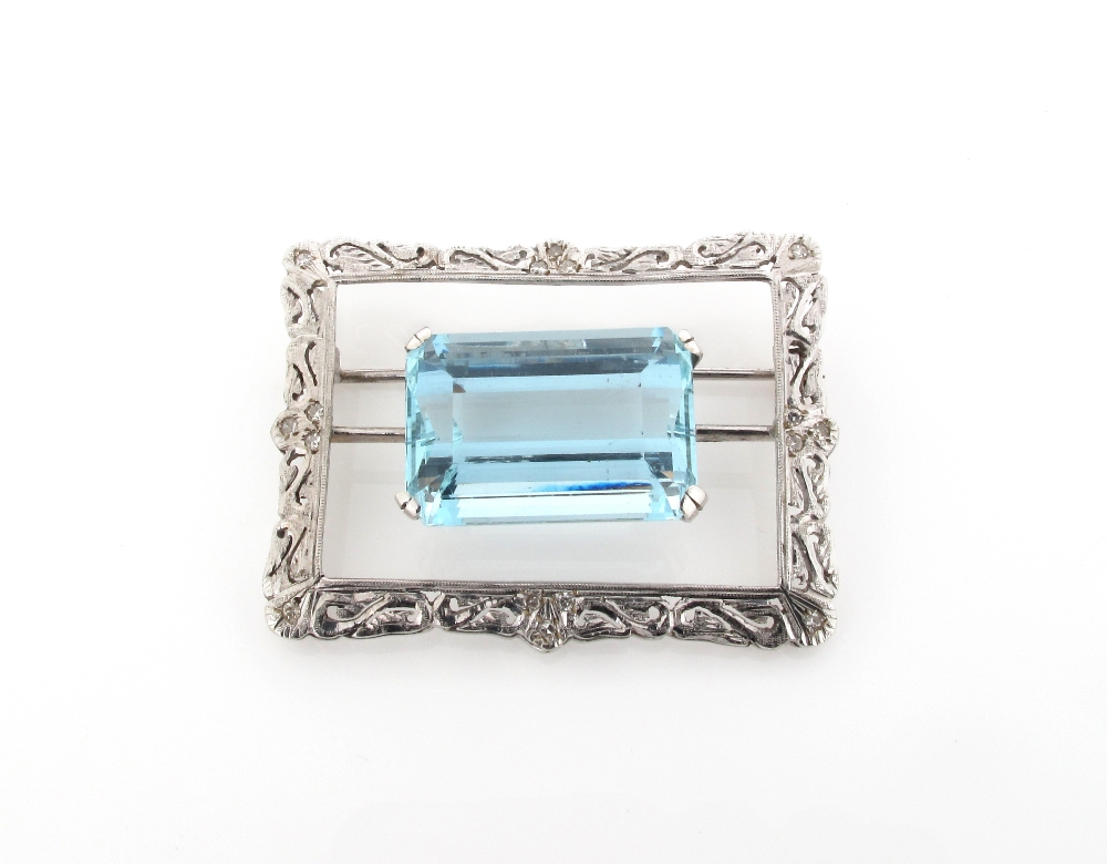 An aquamarine brooch, the emerald cut aquamarine is mounted in pierced and scrolling rectangular