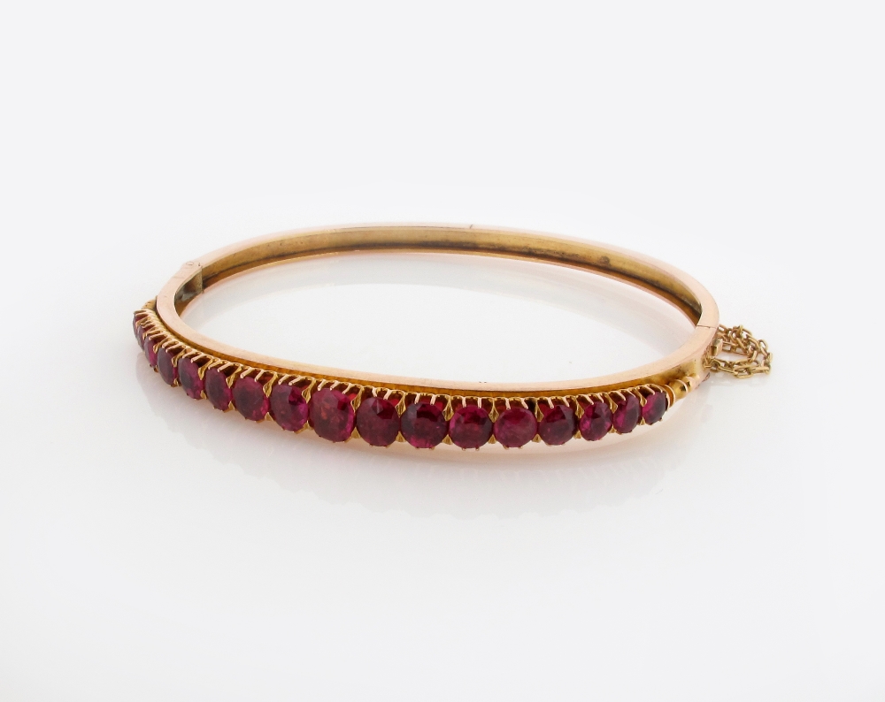 A gold hinged bangle mounted with graduated oval shaped rubies.