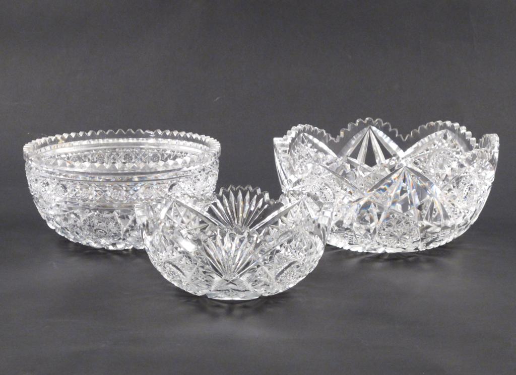 Three large cut glass bowls, two graduated and cut with a lobed rim and a star design, the third