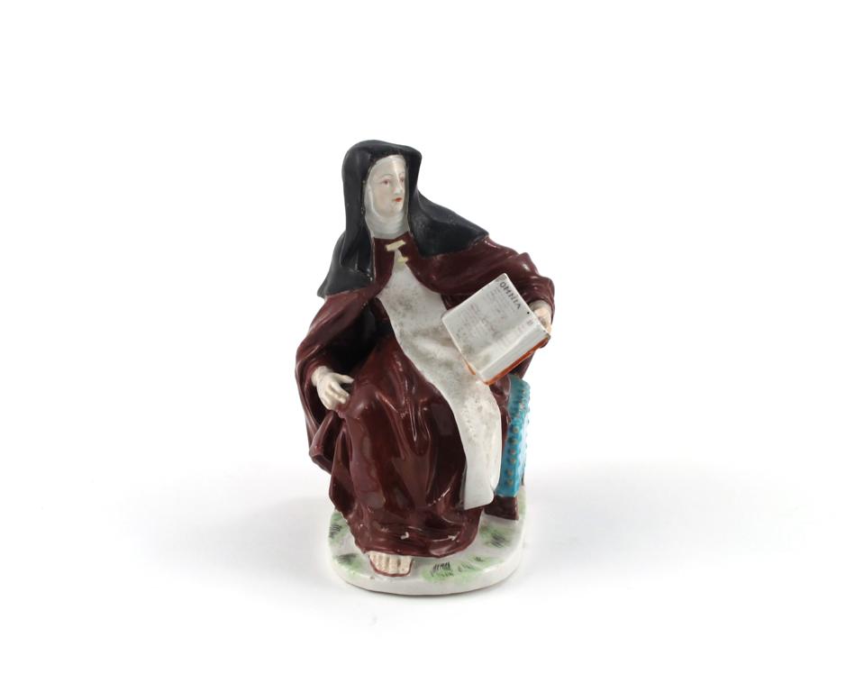 A Derby figure of a nun c.1770, seated on a chest and holding an open book in her left hand,