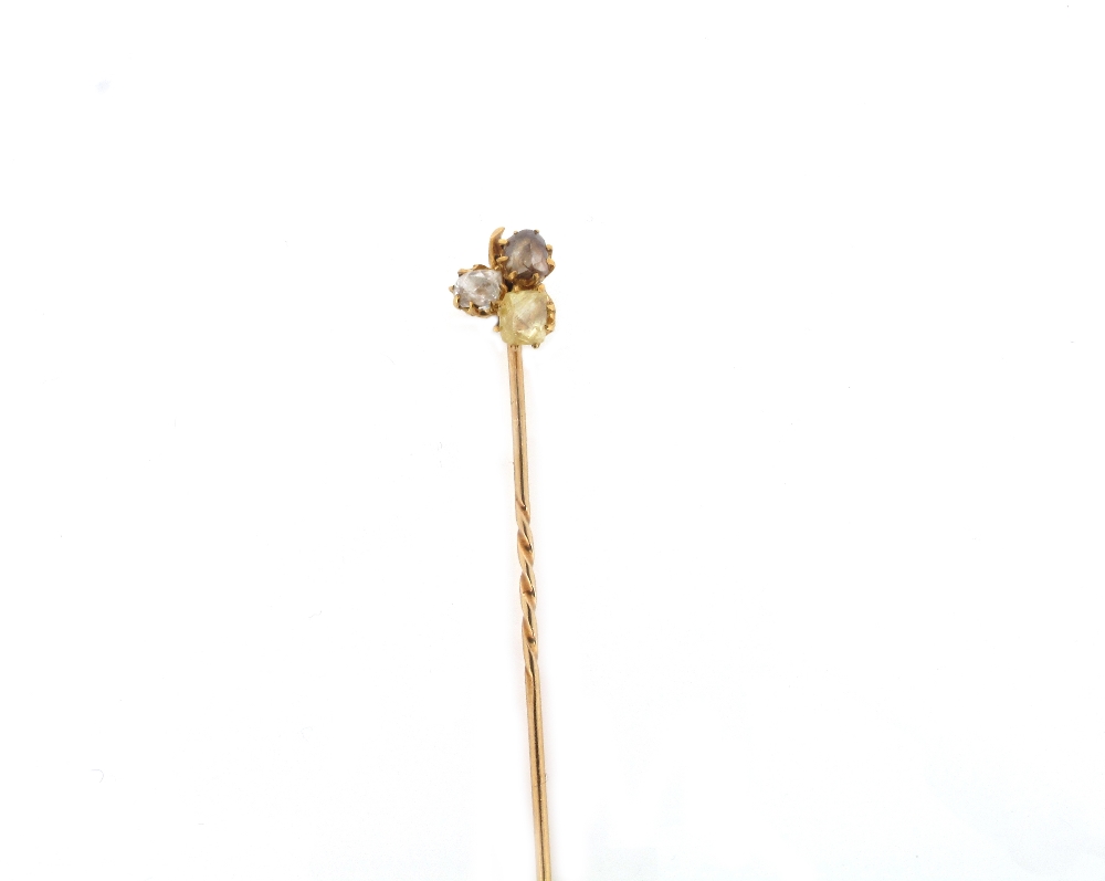 A gold stick pin mounted with three unpolished diamonds.