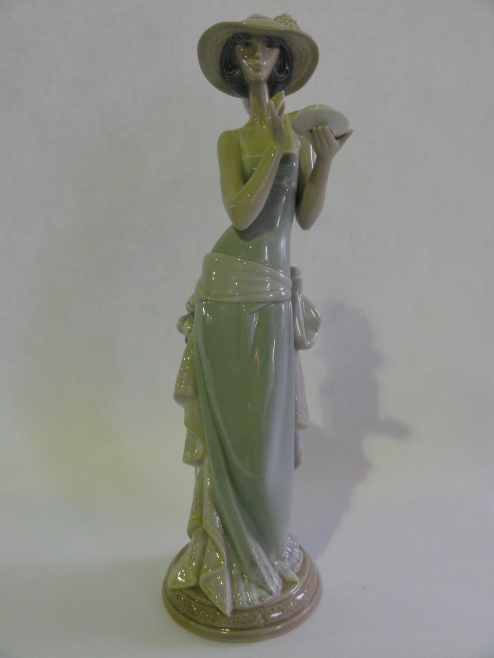 A Lladro figure of a lady stood next to a jardini¦re drinking a cup of tea