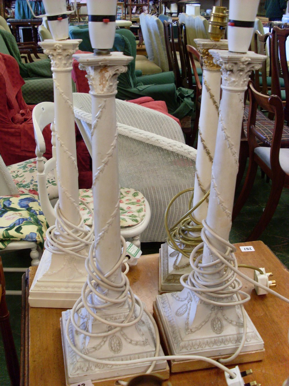 Four white painted table lamps of Adams design with tapering stems and spreading, rectangular bases.