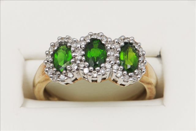 A THREE GREEN STONE RING, surrounded by small eight cut diamonds, three oval centre stones