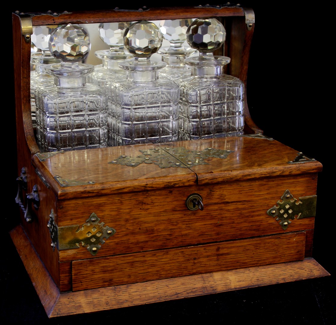 A late 19th/early 20th century brass mounted oak three bottle tantalus/cigarette box, the front with