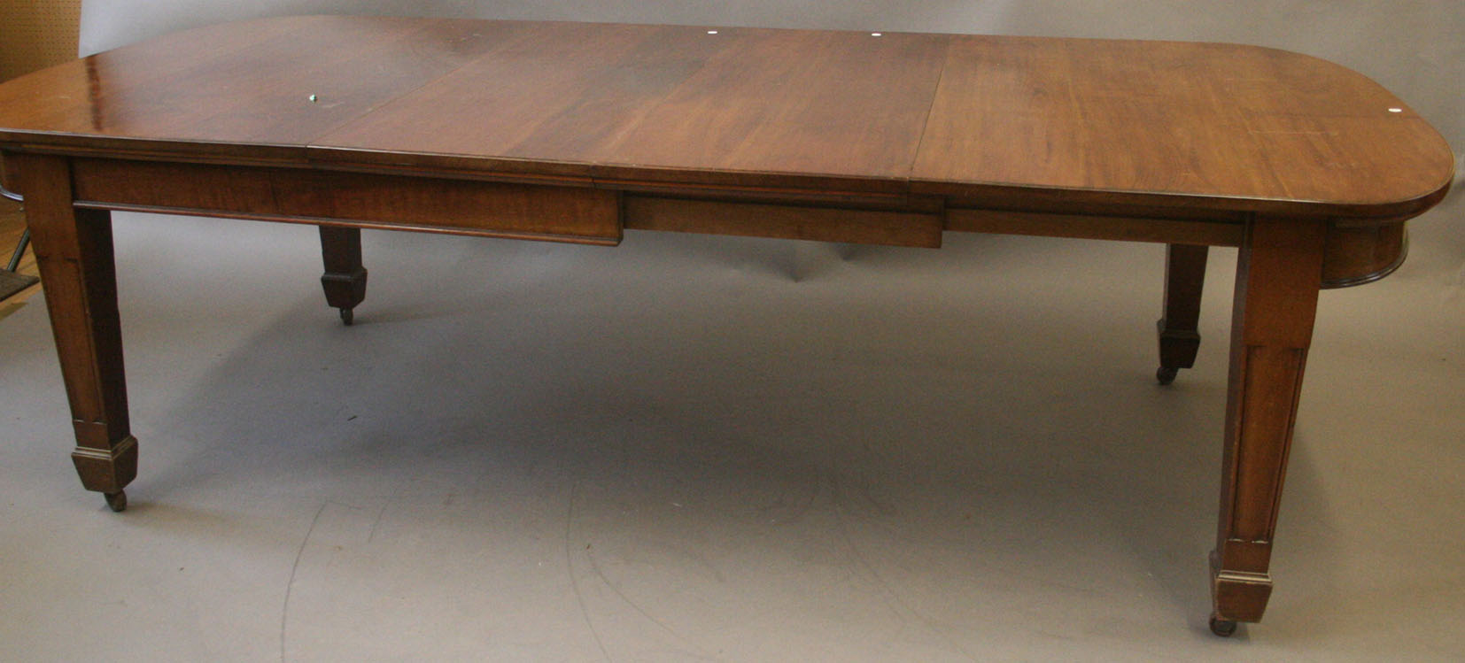 An Edwardian walnut wind-action extending dining table with two extra leaves, raised on square
