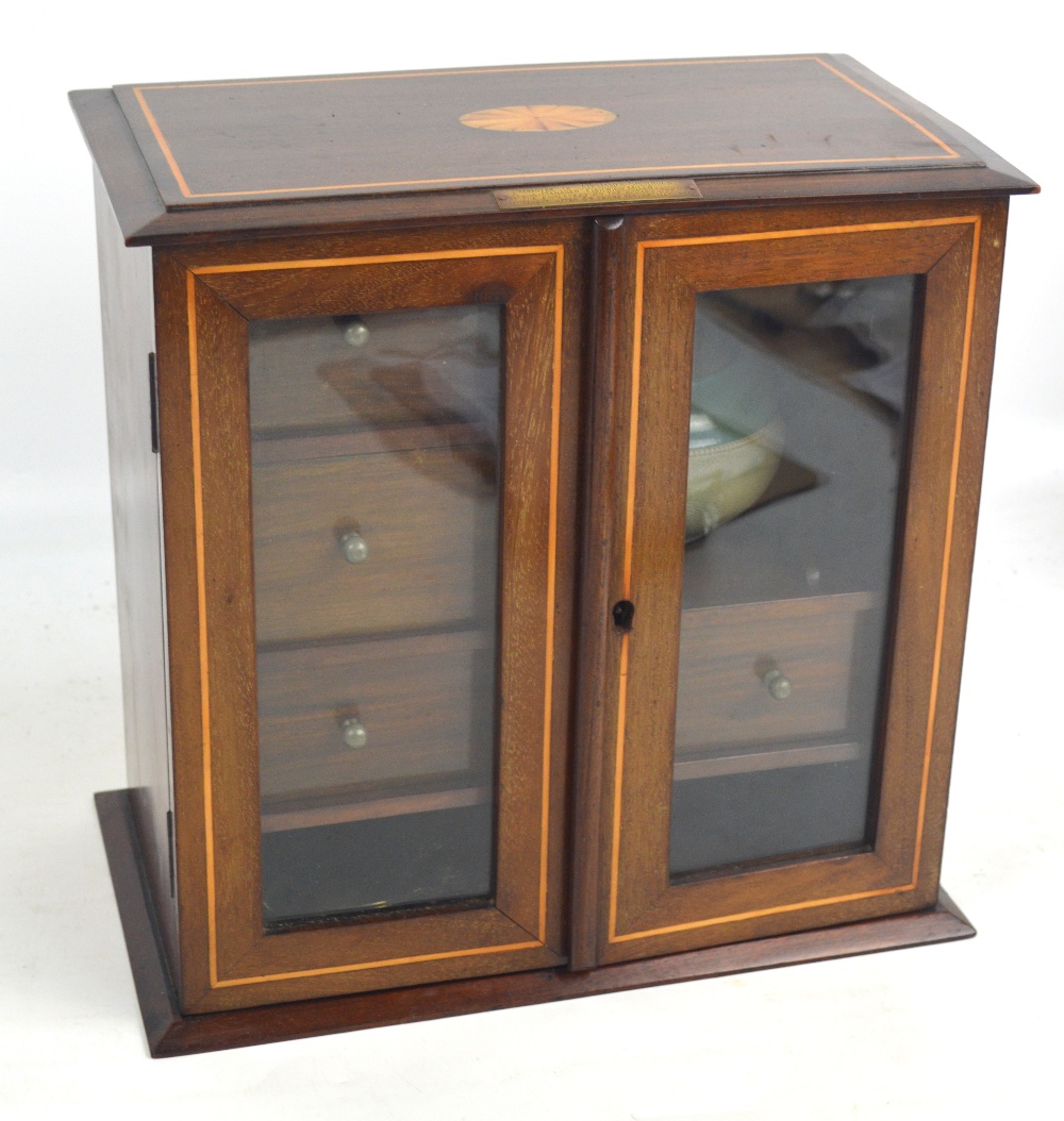 An early 20th century mahogany and inlaid smokers cabinet with two glazed doors opening to reveal an